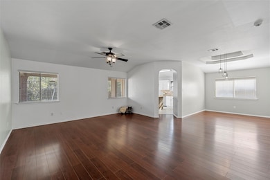 Empty room with arched walkways, dark wood-style flooring, and a ceiling fan