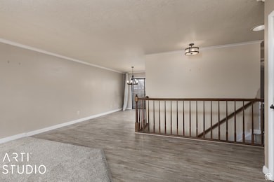 Empty room featuring ornamental molding, a textured ceiling, wood finished floors, and a chandelier