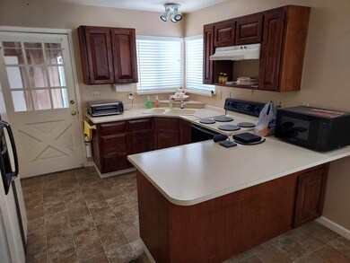 Kitchen with electric stove, under cabinet range hood, black microwave, a peninsula, and light countertops