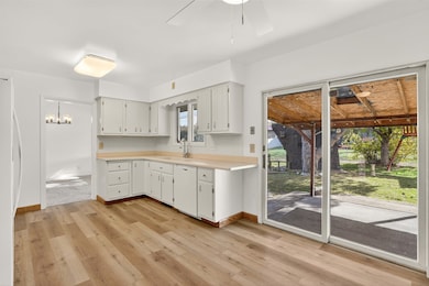 Kitchen featuring light wood finished floors, light countertops, white appliances, white cabinetry, and ceiling fan