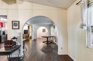 Corridor featuring wood finished floors, a textured ceiling, arched walkways, lofted ceiling, and healthy amount of natural light