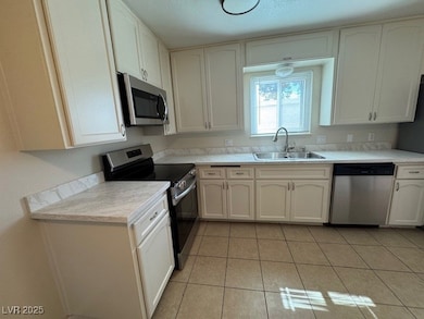 Kitchen featuring stainless steel appliances, light countertops, light tile patterned flooring, and white cabinets