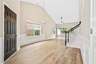 Entryway featuring a ceiling fan, a wainscoted wall, a chandelier, light wood finished floors, and stairs