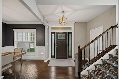 Entrance foyer with dark wood finished floors, wainscoting, a decorative wall, crown molding, and stairway