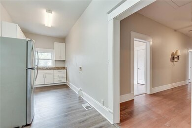 Kitchen with freestanding refrigerator, white cabinets, light wood-style floors, and light stone countertops
