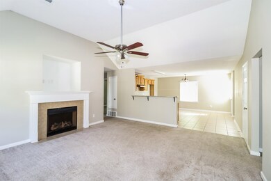 Unfurnished living room with vaulted ceiling, light colored carpet, a tiled fireplace, ceiling fan, and light tile patterned flooring