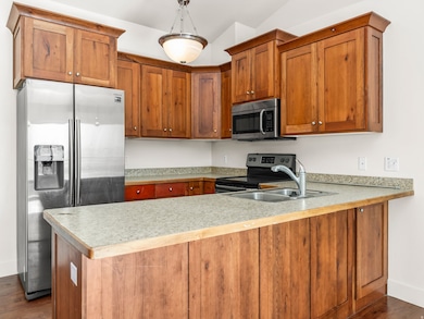 Kitchen featuring dark wood-style flooring, appliances with stainless steel finishes, brown cabinets, light countertops, and vaulted ceiling