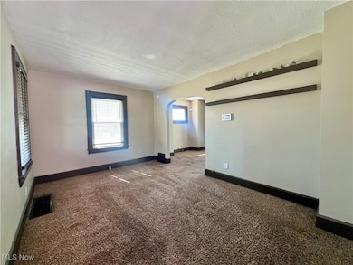 Unfurnished room with dark carpet, a textured ceiling, and arched walkways