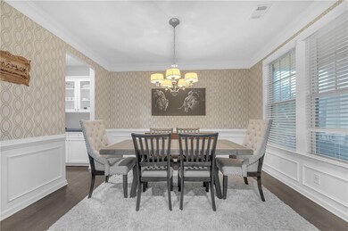 Dining area with wallpapered walls, a chandelier, dark wood finished floors, ornamental molding, and a wainscoted wall