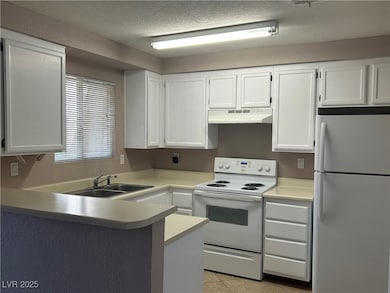 Kitchen featuring white appliances, white cabinetry, light countertops, a peninsula, and a textured ceiling