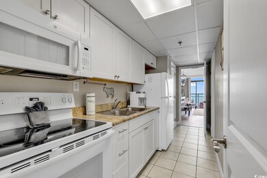 Kitchen with white appliances, a sink, light tile patterned flooring, white cabinetry, and light countertops