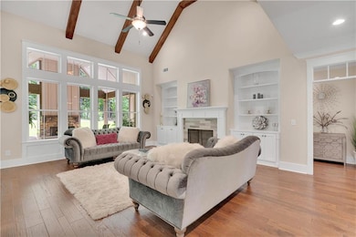 Living room featuring high vaulted ceiling, a fireplace, a ceiling fan, beam ceiling, and wood finished floors