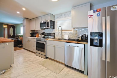 Kitchen with wooden counters, appliances with stainless steel finishes, decorative backsplash, gray cabinetry, and light marble finish floors