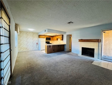 Unfurnished living room with light colored carpet, a textured ceiling, a fireplace, and wallpapered walls