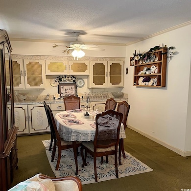 Dining area with a textured ceiling, ceiling fan, baseboards, dark colored carpet, and crown molding
