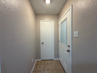 Doorway to outside with a textured wall, a textured ceiling, and tile patterned flooring