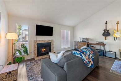 Living room featuring vaulted ceiling, wood finished floors, and a tile fireplace
