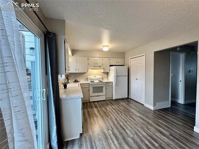Kitchen featuring white appliances, a textured ceiling, light countertops, under cabinet range hood, and dark wood-style flooring