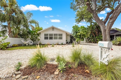 Front Elevation – This charming 1925 bungalow makes a great first impression with tropical landscaping, a wide circular shell drive, and a private seating area nestled under mature palms.