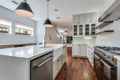 Kitchen featuring range with two ovens, range hood, dishwasher, dark wood-style floors, and light stone counters
