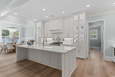 Kitchen with range, crown molding, an island with sink, white cabinets, and a sink