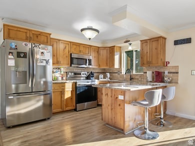 Kitchen with stainless steel appliances, a kitchen bar, backsplash, light stone counters, and crown molding