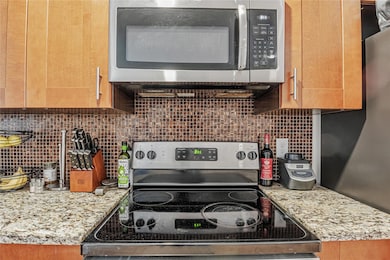 Kitchen featuring stainless steel appliances, decorative backsplash, and light stone counters