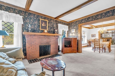 Carpeted living room with beamed ceiling, wallpapered walls, a fireplace, and a chandelier