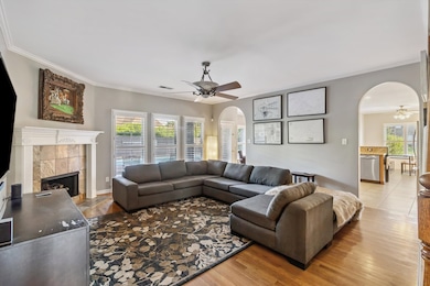 Living area with a ceiling fan, arched walkways, ornamental molding, and a tiled fireplace