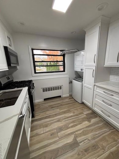 Kitchen featuring white cabinets, range, radiator heating unit, and estacked washer and dryer