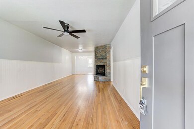 Unfurnished living room featuring light wood-style flooring, a ceiling fan, a stone fireplace, and wainscoting