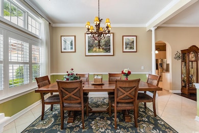 Dining room with light tile patterned flooring, arched walkways, ornamental molding, a chandelier, and decorative columns