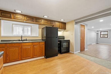 Kitchen featuring light wood-type flooring, black appliances, brown cabinetry, dark countertops, and recessed lighting