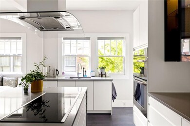 Kitchen with white cabinets, extractor fan, black electric stovetop, double oven, and modern cabinets