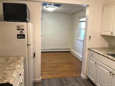 Kitchen featuring freestanding refrigerator, light stone countertops, white cabinets, dark wood-style floors, and a paneled ceiling