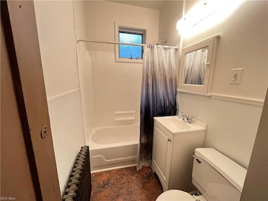 Full bathroom with tile flooring, radiator heating unit, toilet, vanity with extensive cabinet space, and shower / tub combo with curtain