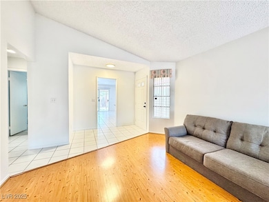 Living area featuring lofted ceiling, light wood-style flooring, and a textured ceiling