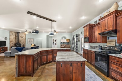 Kitchen featuring black appliances, a wood stove, open floor plan, ornamental molding, and finished concrete floors