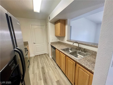Kitchen with stainless steel appliances, light wood finished floors, a textured ceiling, and granite countertops