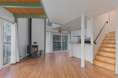 Stairway with wood finished floors, a wood stove, and beamed ceiling