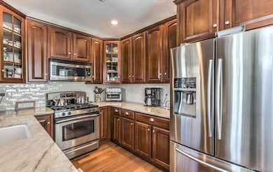 Kitchen featuring stainless steel appliances, glass insert cabinets, light stone counters, backsplash, and light wood-type flooring