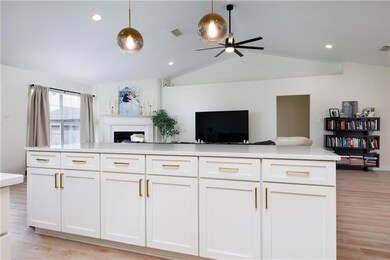 Kitchen with open floor plan, ceiling fan, white cabinets, light countertops, and light wood-style flooring