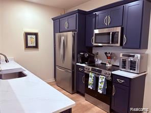 Kitchen featuring light countertops, appliances with stainless steel finishes, blue cabinetry, and light wood-style flooring