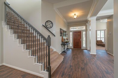 Surrounded by sunlit transom windows, the solid mahogany front door leads into this inviting foyer boasting wood-inspired ceramic tile flooring, double crown molding, updated lighting, neutral paint, and handsome columns adorned with custom millwork.