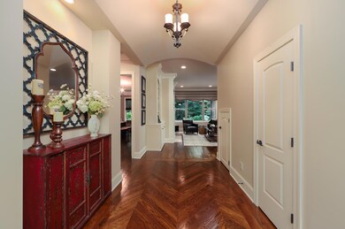 Gorgeous foyer boasts hardwoods in a chevron pattern while oversized windows beyond the living room provide a lovely view of the woods. 