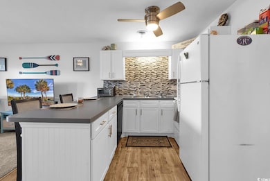 Kitchen featuring dark countertops, freestanding refrigerator, a peninsula, tasteful backsplash, and white cabinetry