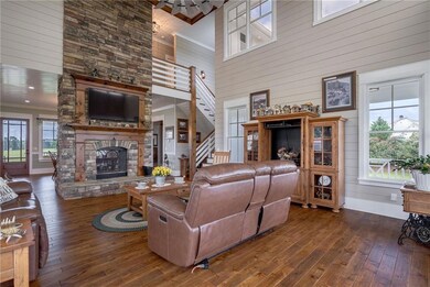 Living area featuring a high ceiling, stairway, a stone fireplace, hardwood / wood-style flooring, and plenty of natural light