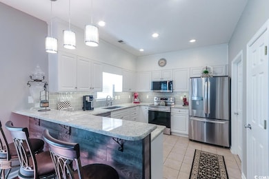 Kitchen featuring stainless steel appliances, a peninsula, white cabinetry, a breakfast bar area, and tasteful backsplash