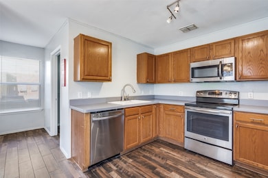 Kitchen with appliances with stainless steel finishes, dark wood-style flooring, brown cabinetry, light countertops, and rail lighting