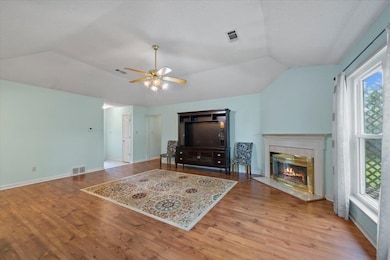 Living room featuring vaulted ceiling, ceiling fan, a glass covered fireplace, wood finished floors, and healthy amount of natural light